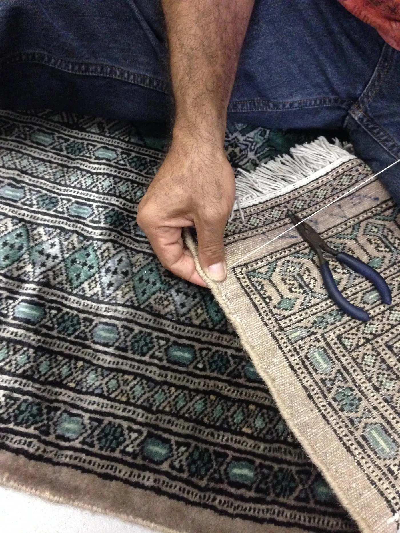 Hands repairing the woven foundation of a Persian rug at the bench